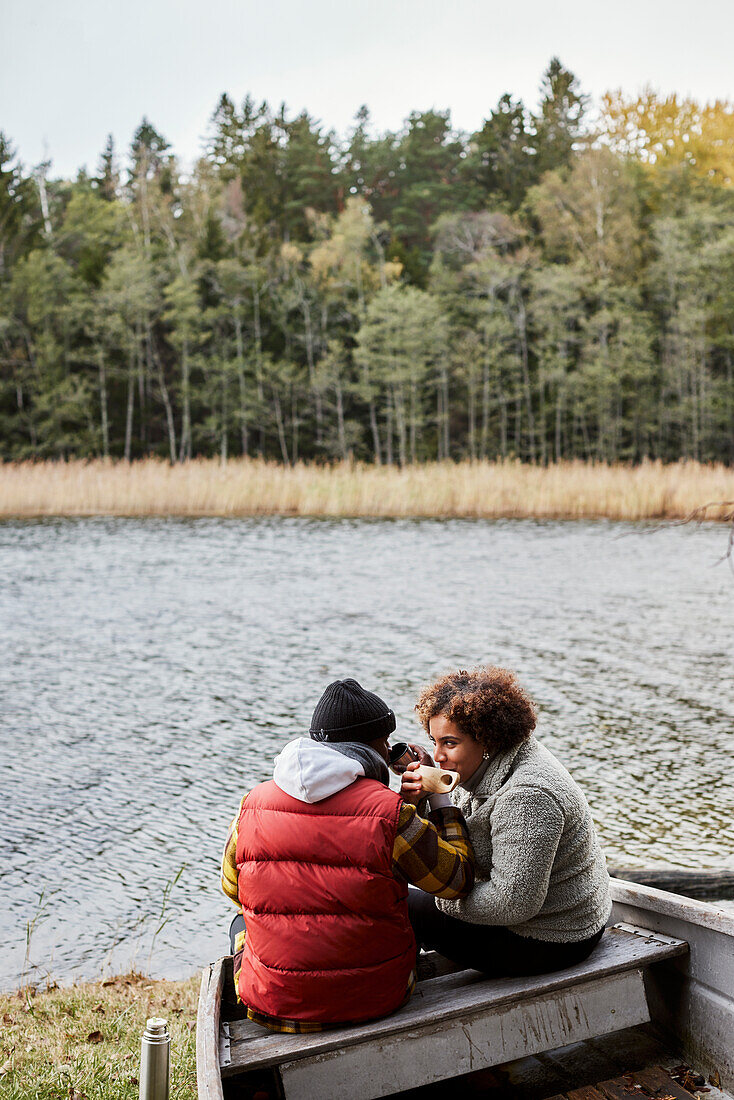 Friends sitting on old boat and drinking by lake