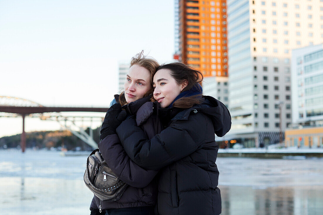 Junge Frauen, die im Winter am Fluss stehen und sich umarmen