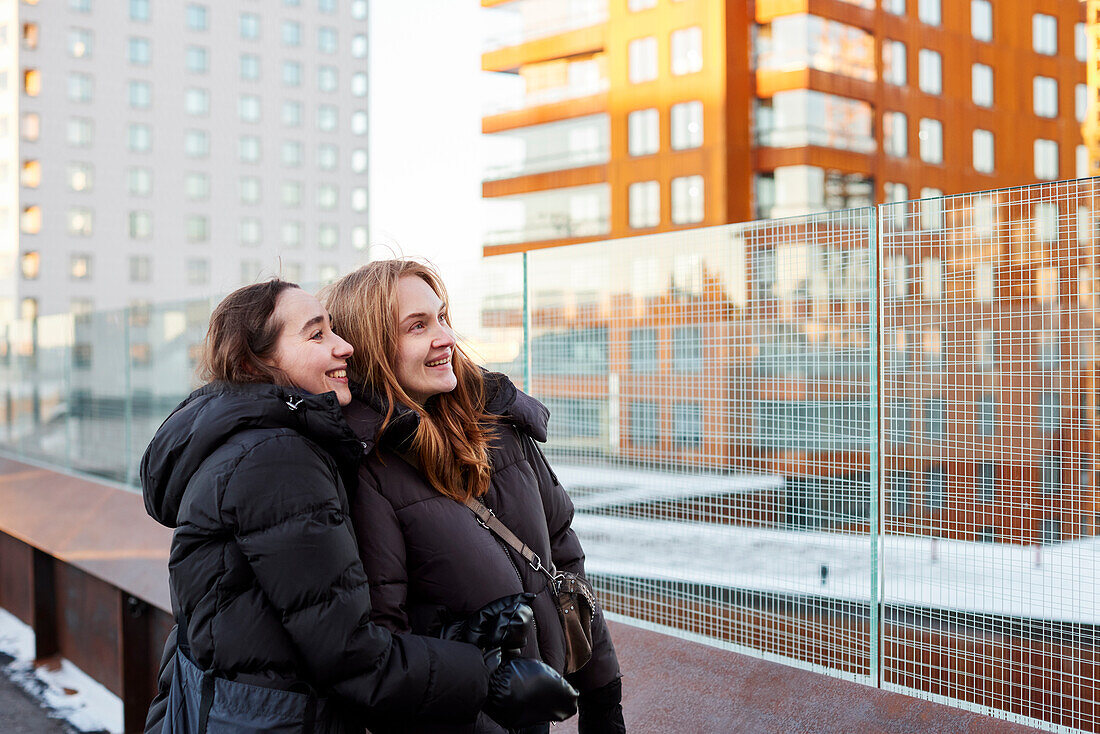 Lächelndes weibliches Paar mit Blick auf moderne Wohngebäude