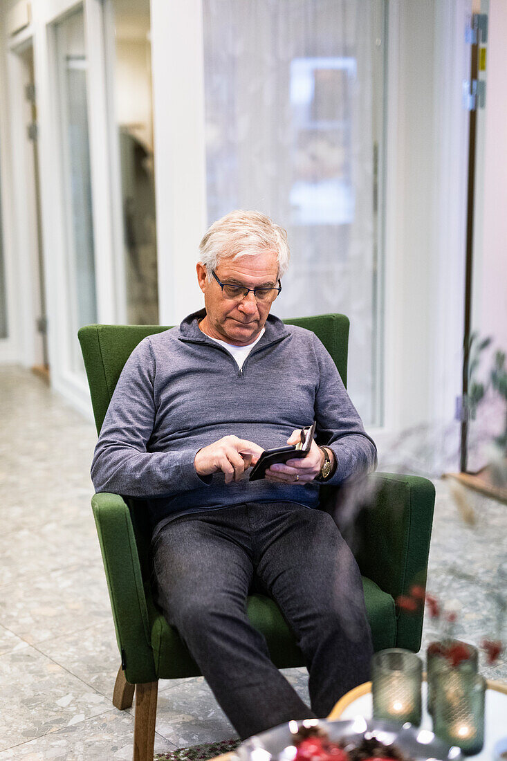 Älterer Mann sitzt im Sessel und benutzt sein Smartphone