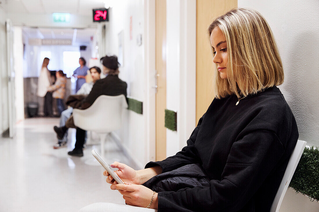 Junge Patientin, die in der Ambulanz wartet und ihr Smartphone benutzt