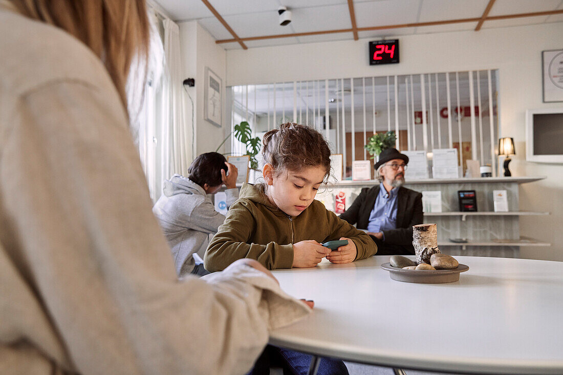 Mädchen im Wartezimmer, das ein Mobiltelefon benutzt