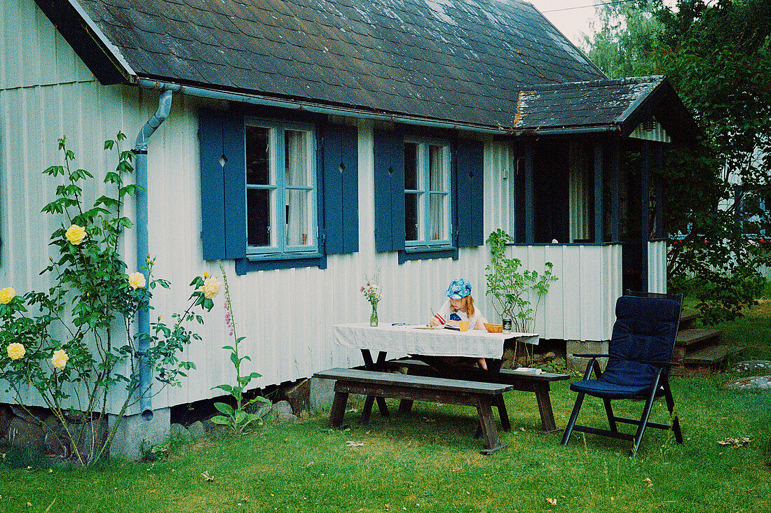 Girl sitting at table in front of wooden house