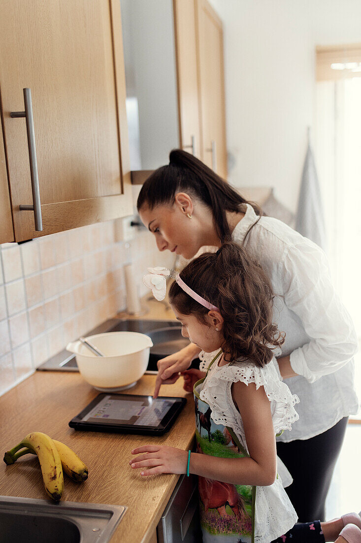 Mother and daughter in kitchen using tablet while baking