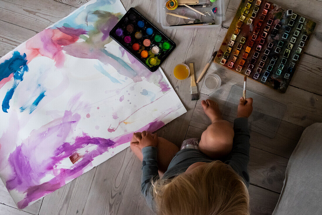 Junge sitzt auf dem Boden und malt mit Wasserfarben