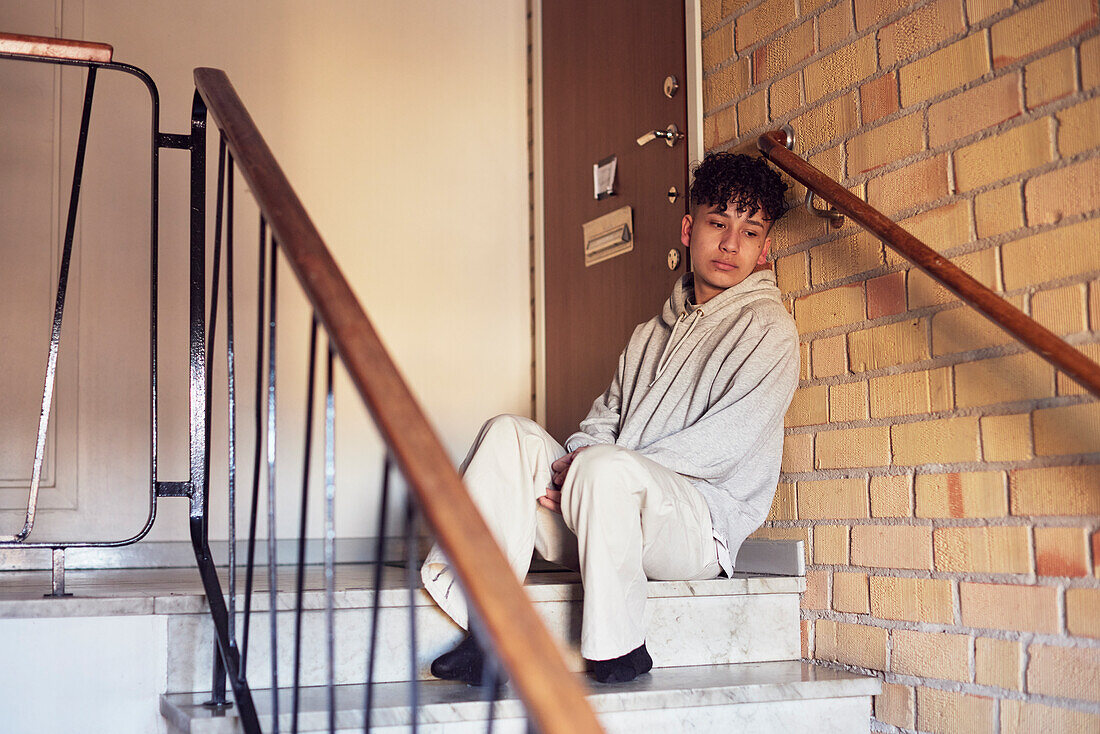 Junge sitzt auf einer Treppe und lehnt sich an eine Wand
