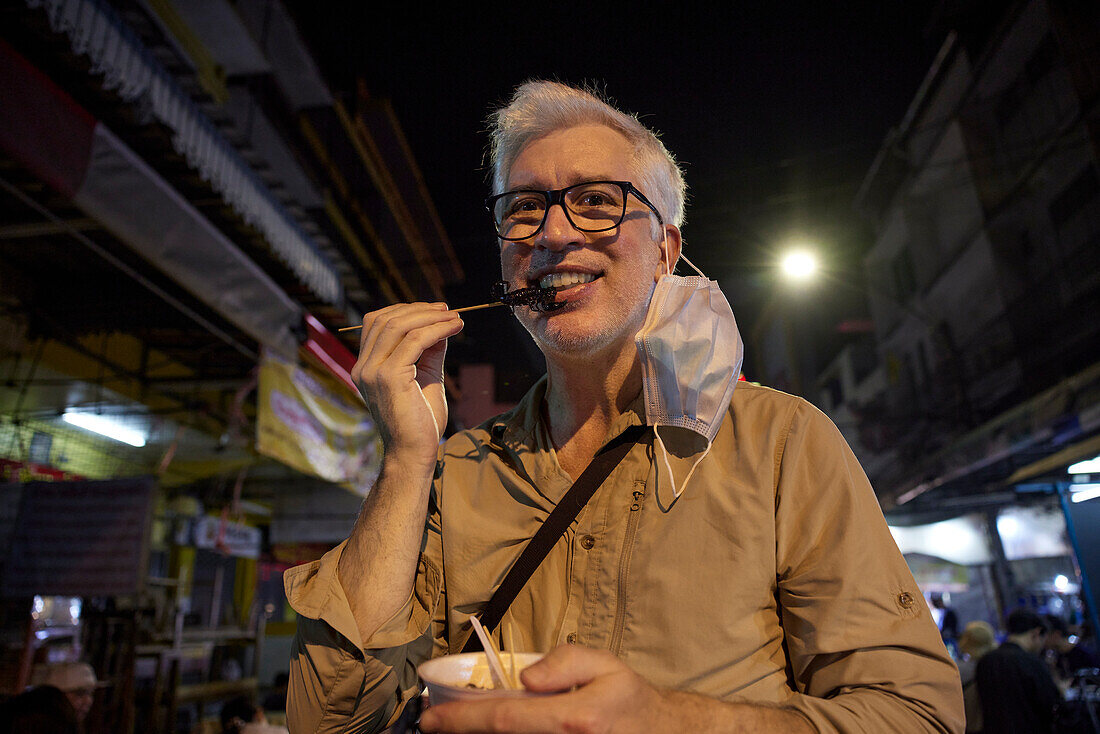 Porträt eines lächelnden älteren Mannes, der Straßenessen isst