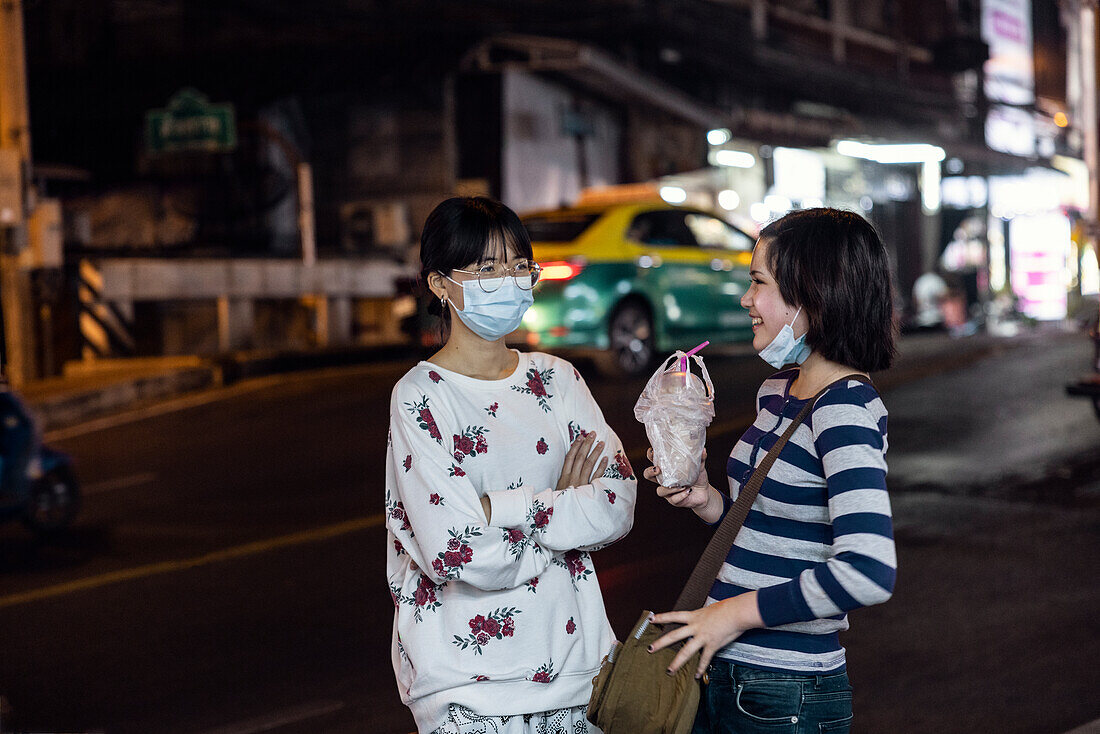 Junge Frauen mit Gesichtsmasken unterhalten sich auf der Straße
