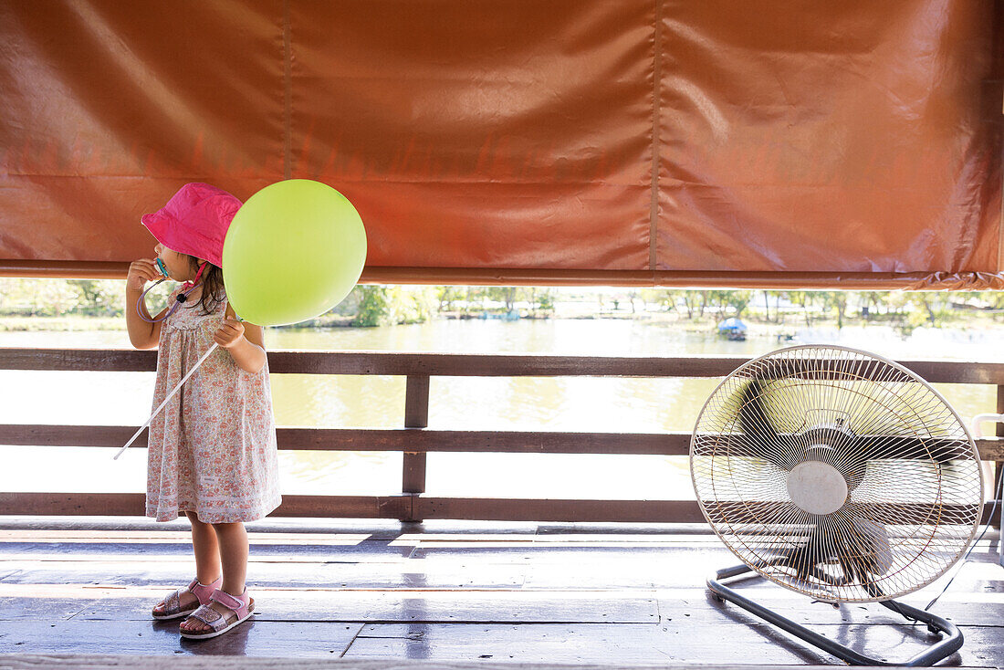 Girl holding balloon next to electric fan