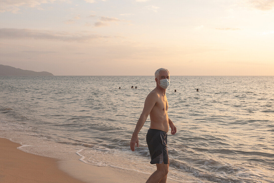 Senior man walking on beach in protective face mask