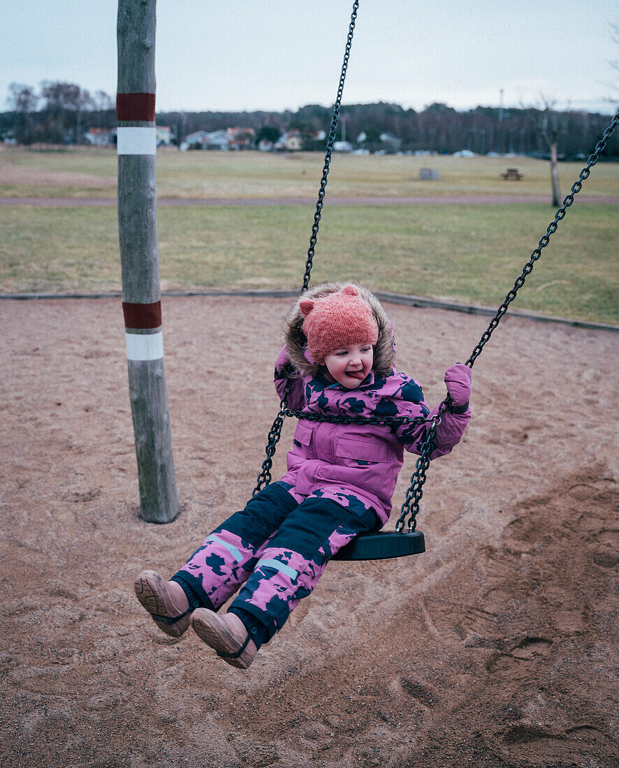 Girl in pink winter clothes swinging on swing
