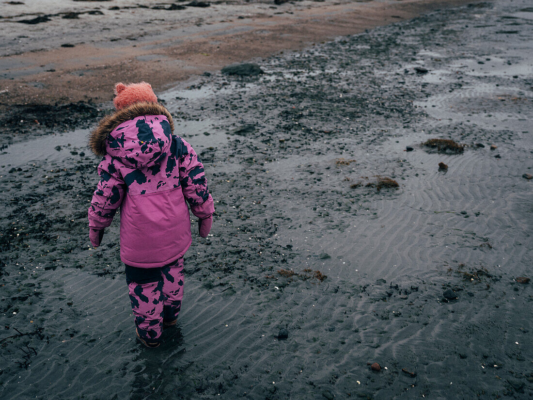 Girl in pink winter clothes walking in mud