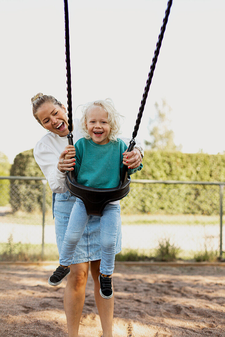 Happy mother swinging child at playground