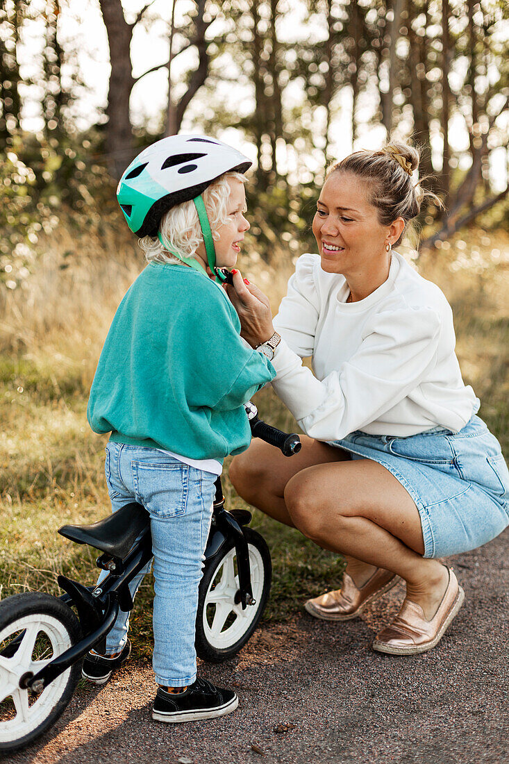 Mother helping child to put cycling helmet on