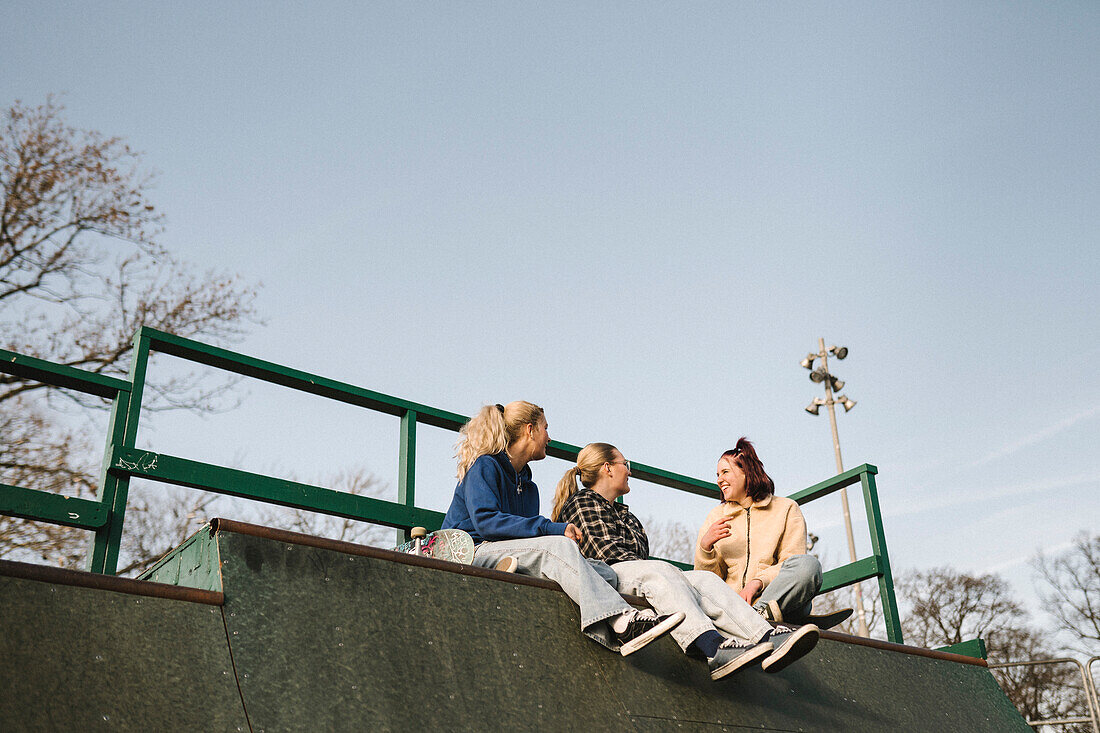 Lächelnde Teenager-Mädchen sitzen im Skatepark