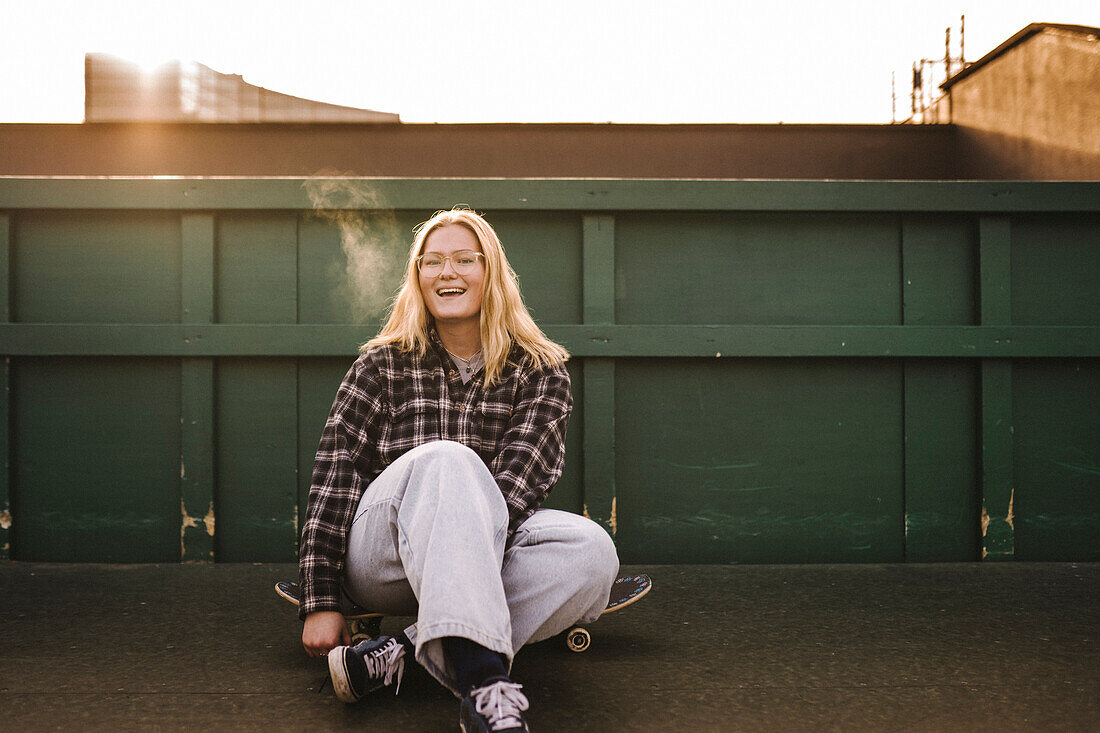 Porträt eines lächelnden Teenager-Mädchens, das auf einem Skateboard sitzt