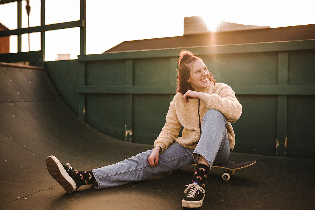 Smiling teenage girl sitting on skateboard