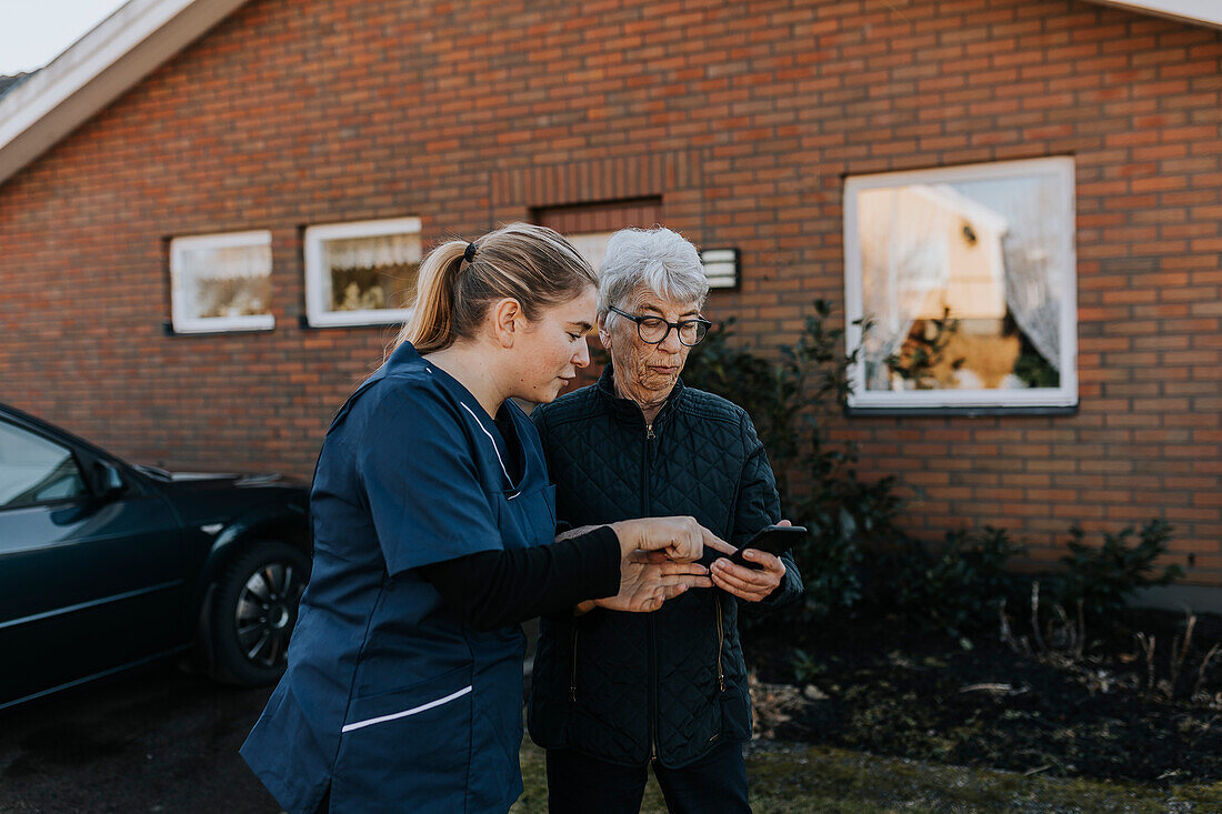 Home caretaker helping senior woman use phone