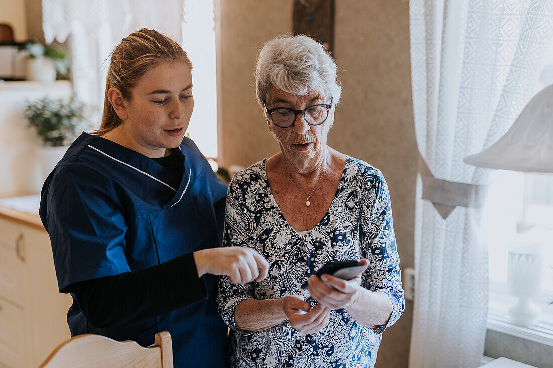 Home caretaker helping senior woman use smart phone