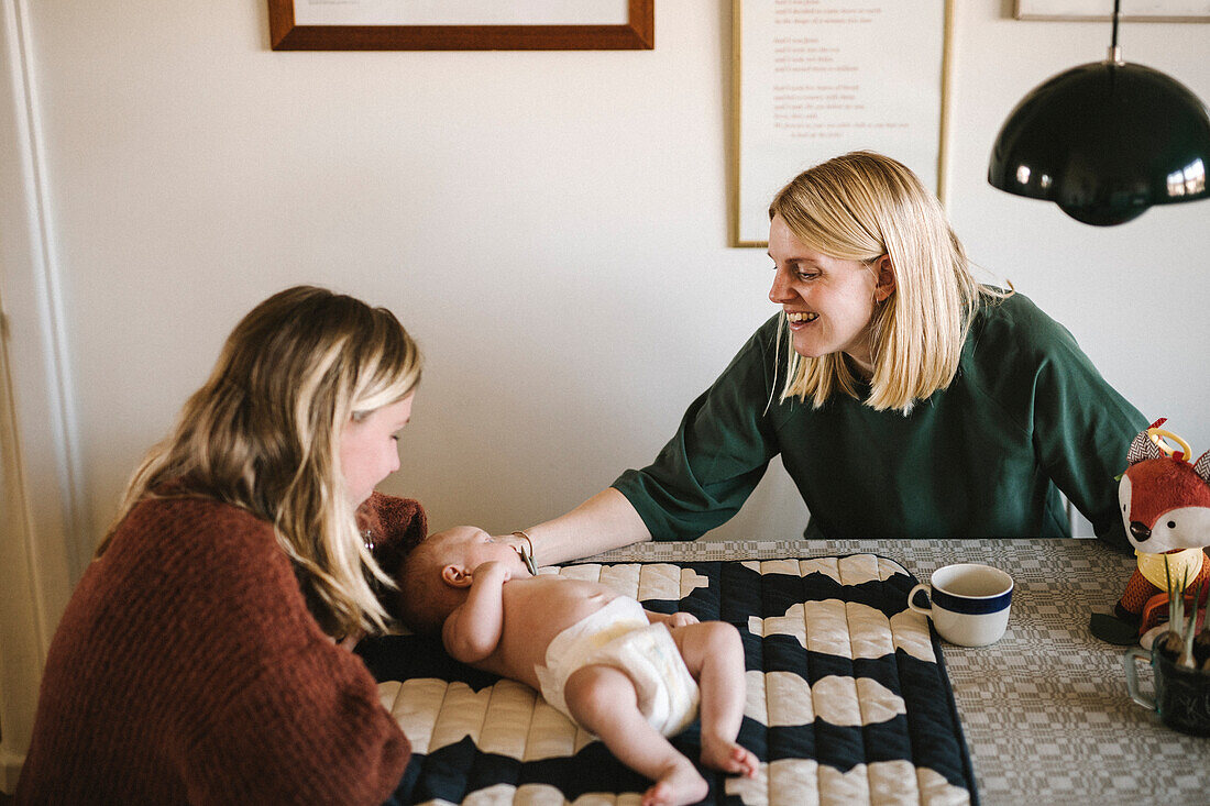 Lächelnde Mütter entspannen sich zu Hause mit neugeborenem Baby