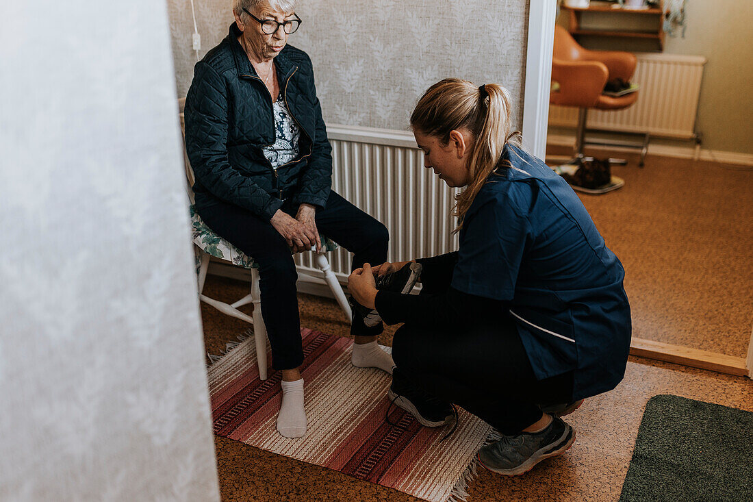 Home caretaker helping senior woman put on shoes