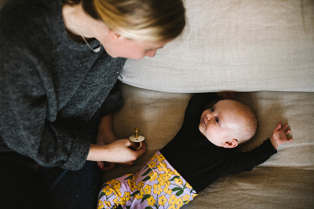 Mutter sitzt neben neugeborenem Baby auf dem Sofa