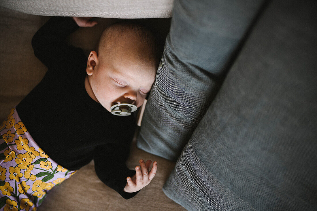 Newborn baby with pacifier sleeping on sofa