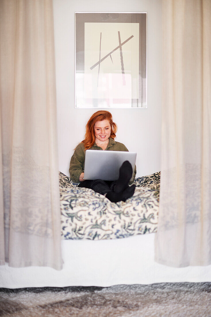 Smiling woman using laptop on bed