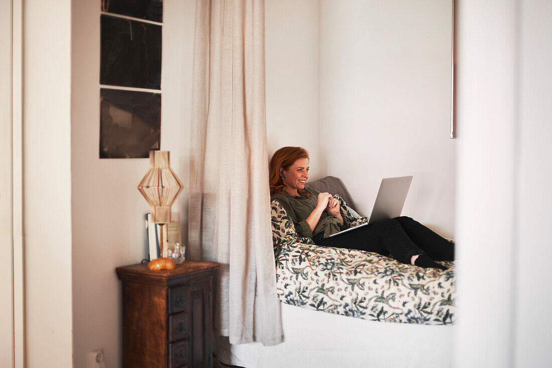 Smiling woman using laptop on bed