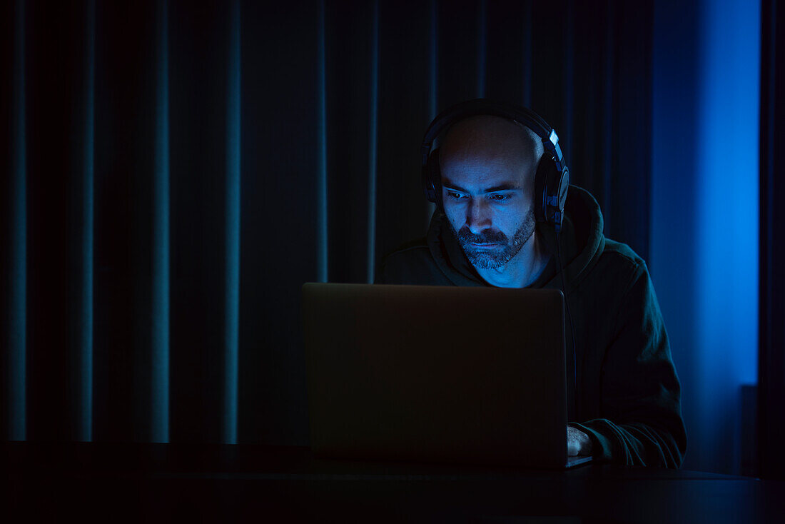 Mann arbeitet am Laptop in einem dunklen Büro