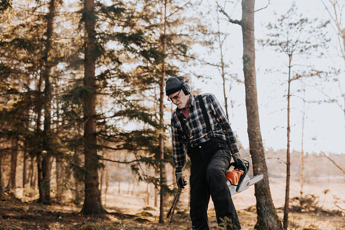 Senior man in forest holding chainsaw