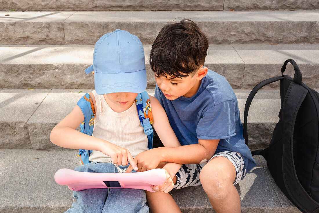 Kinder, die auf einer Treppe sitzen und ein Tablet benutzen