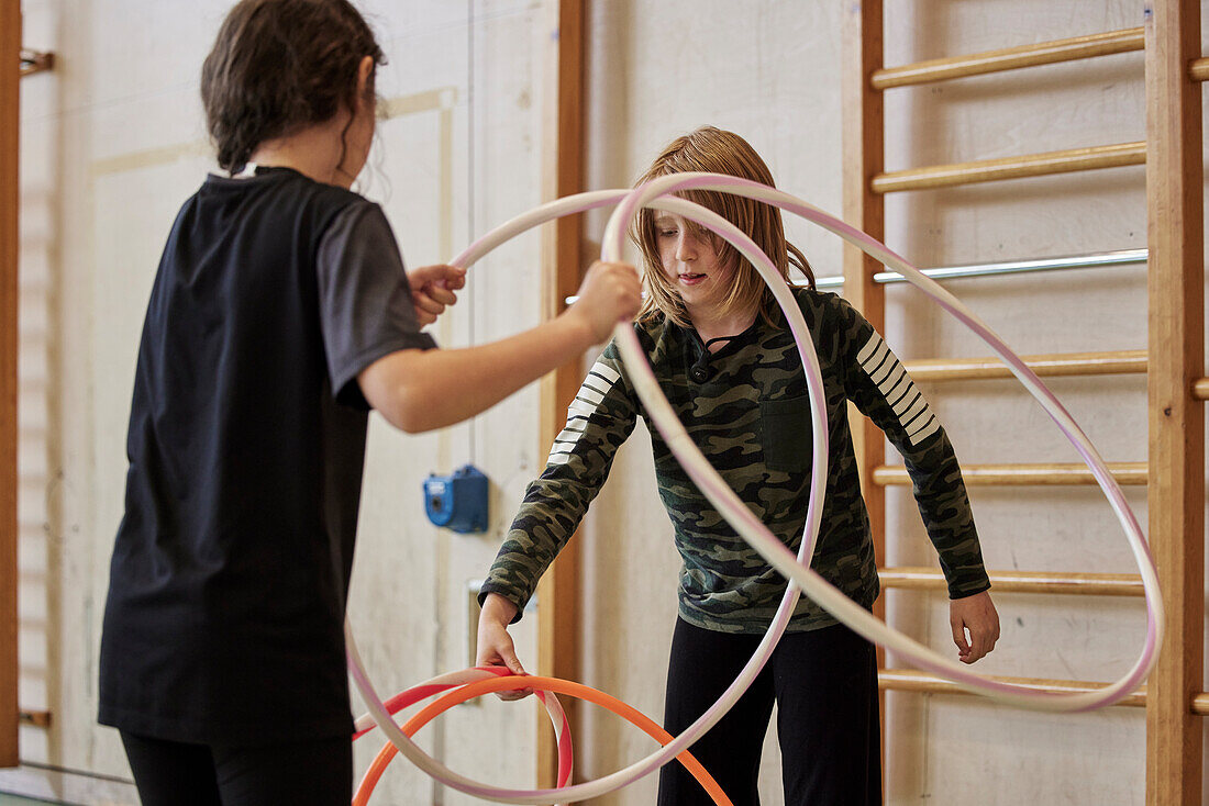 Kinder spielen mit Hula-Hoop-Reifen in der Schulturnhalle