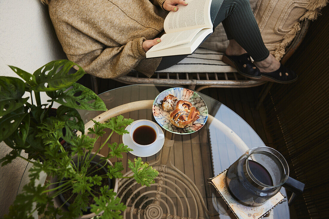 Frau liest ein Buch und trinkt Tee und isst einen Snack