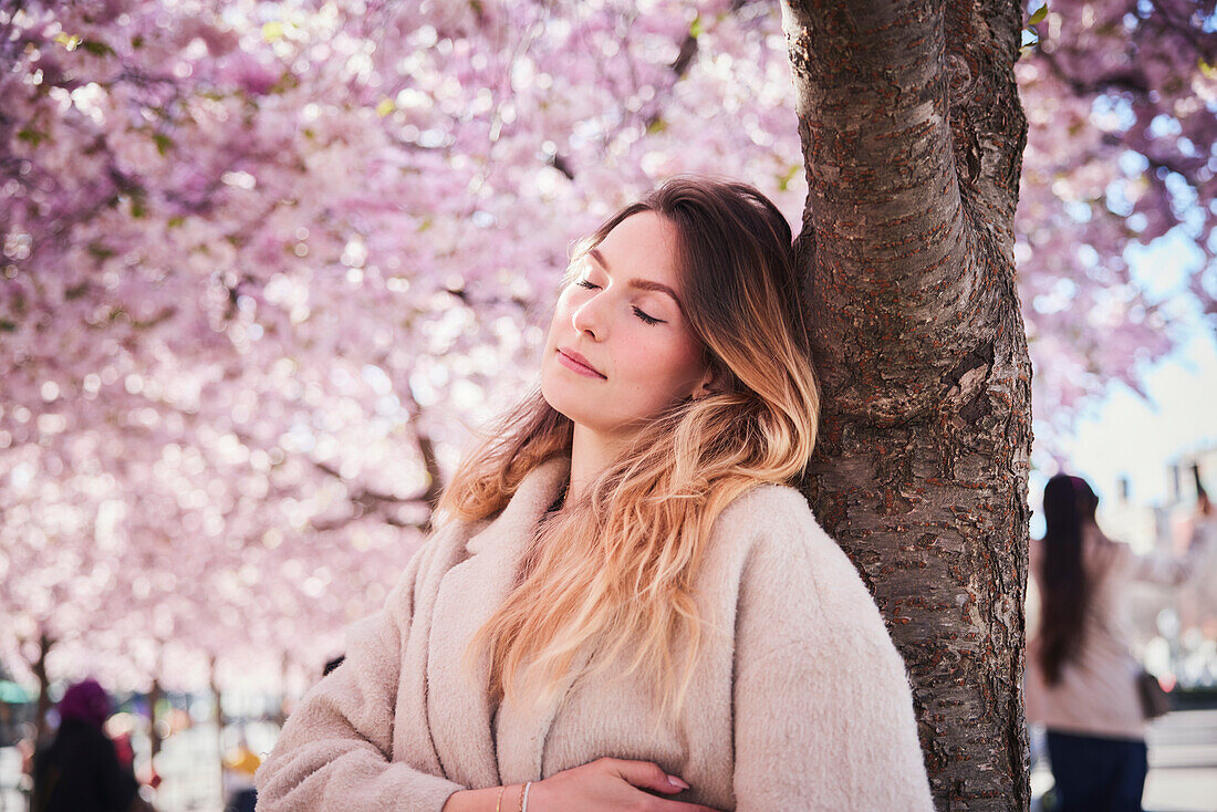 Junge Frau steht unter einer Kirschblüte