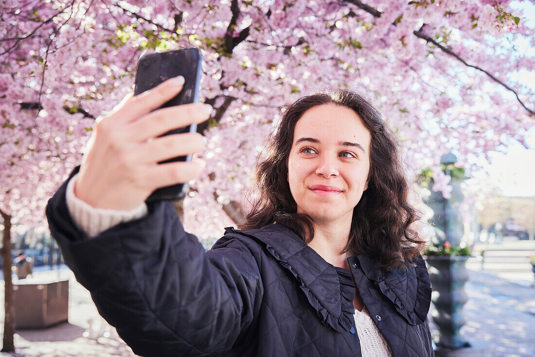 Junge Frau macht ein Selfie vor Kirschbäumen