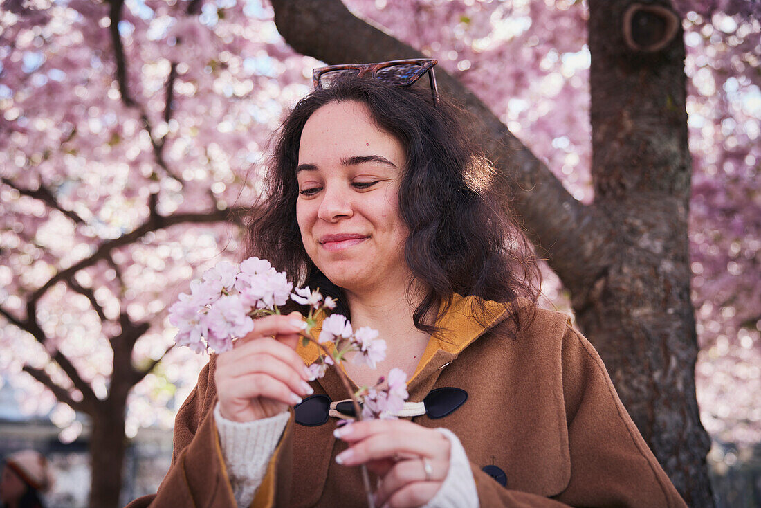 Young woman standing under cherry blossom and holding branch