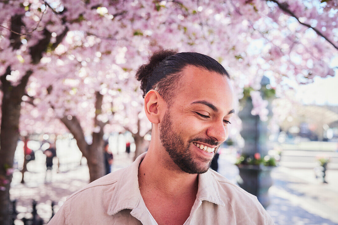 Lächelnder junger Mann unter einer Kirschblüte stehend