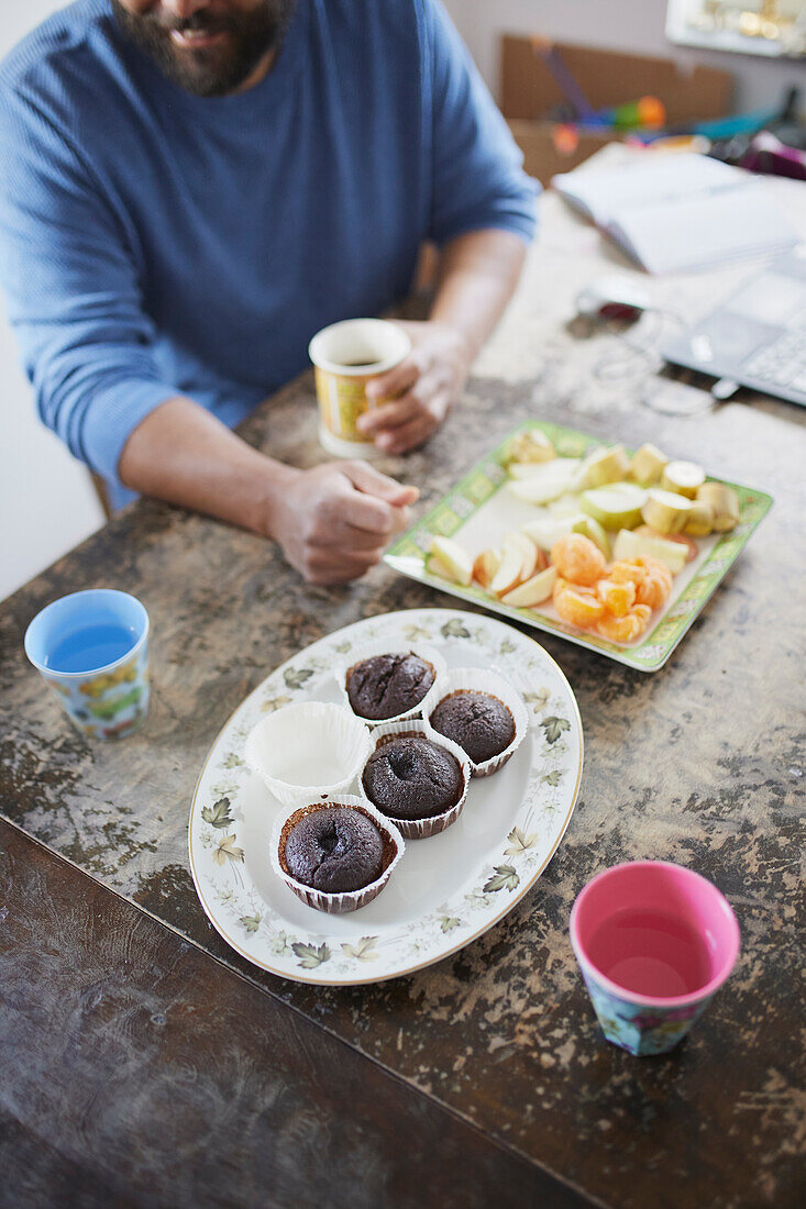 Man sitting at table and having fruit and cupcakes