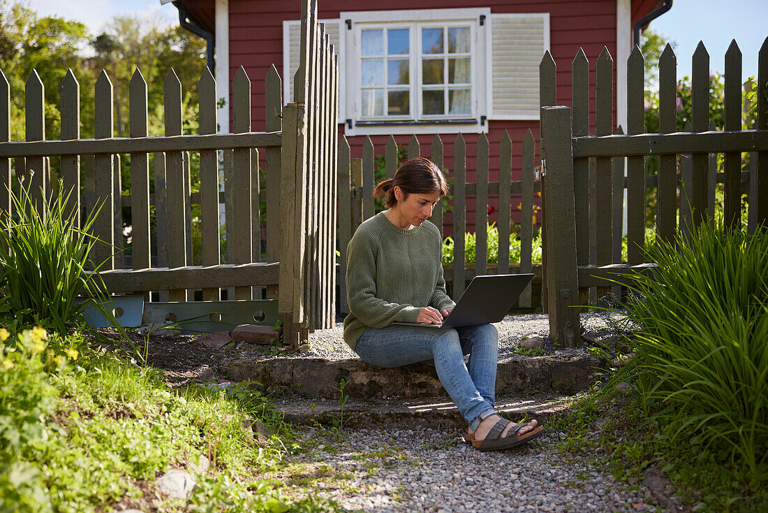 Frau mit Laptop vor einem Holzhaus