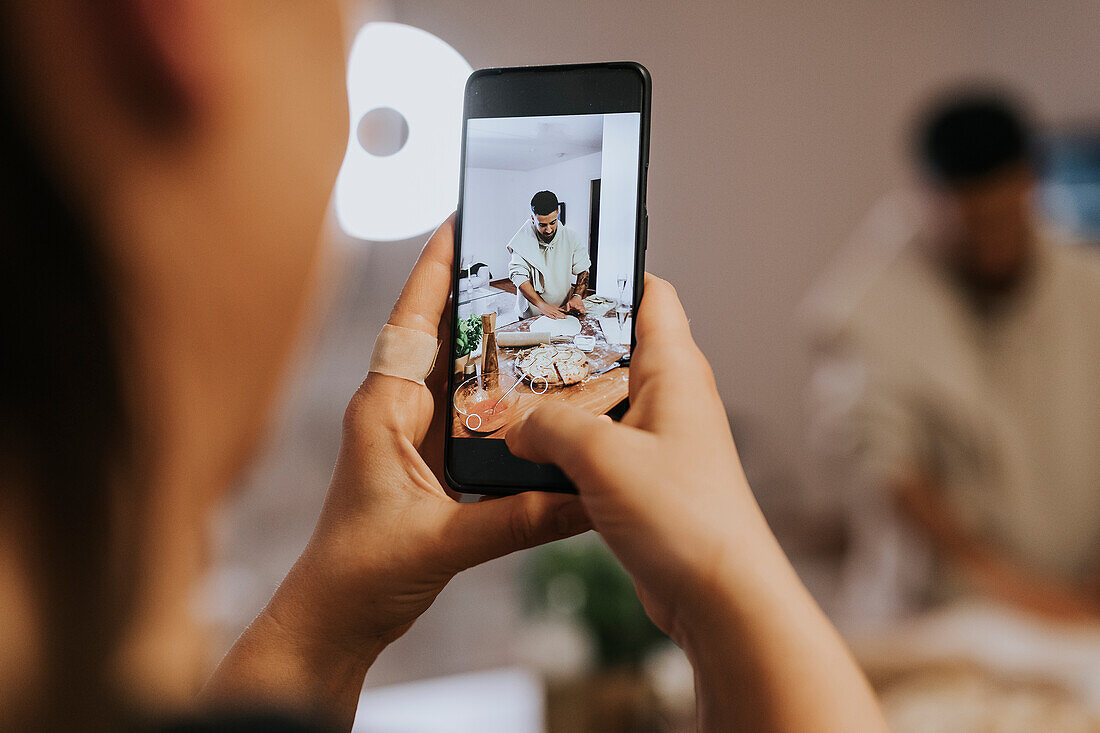 Hand mit Handy fotografiert Mann bei der Essenszubereitung