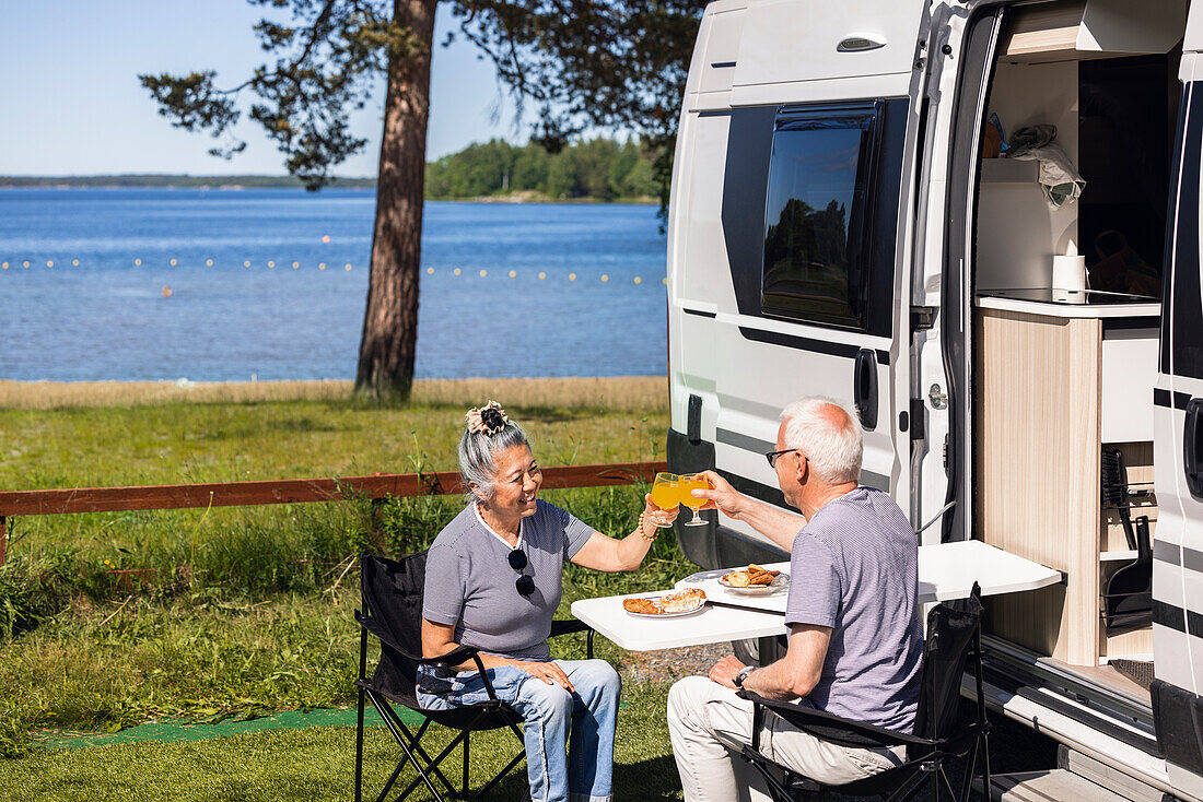 Senior couple having meal and rising toast at camp site