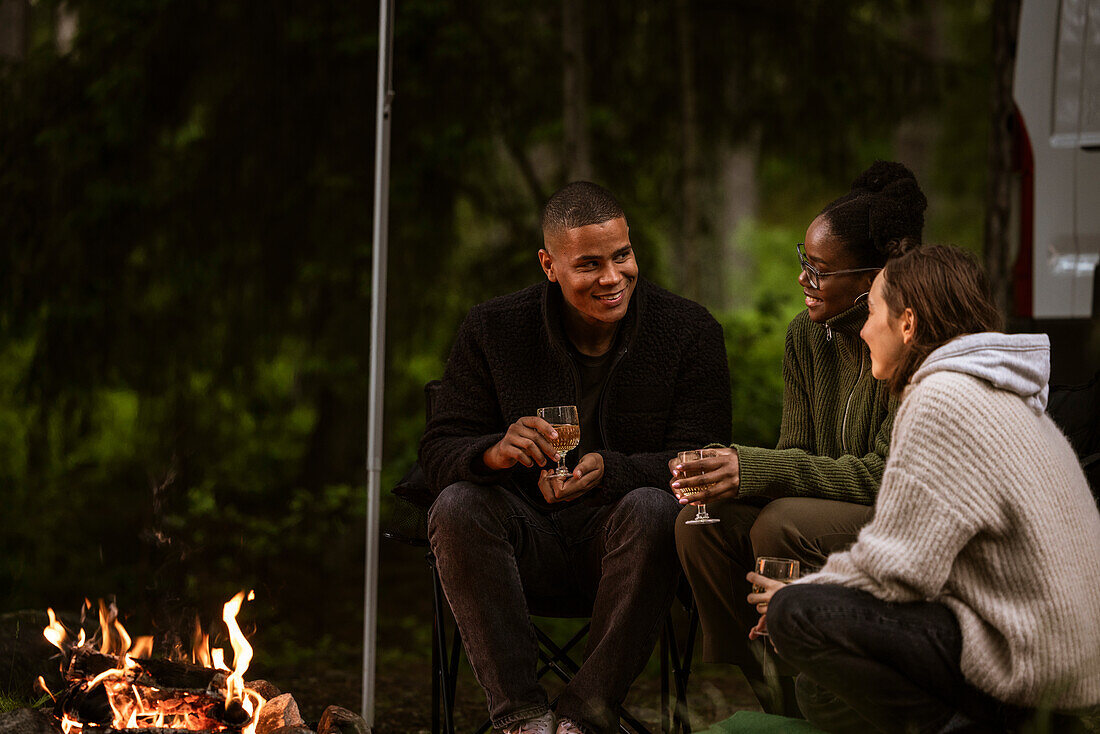 Friends sitting by campfire and drinking wine
