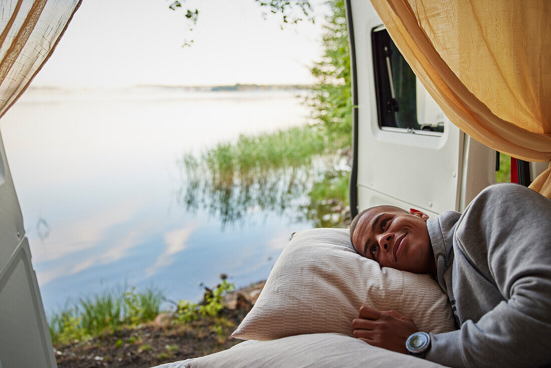 Man lying in camper van and looking at lake