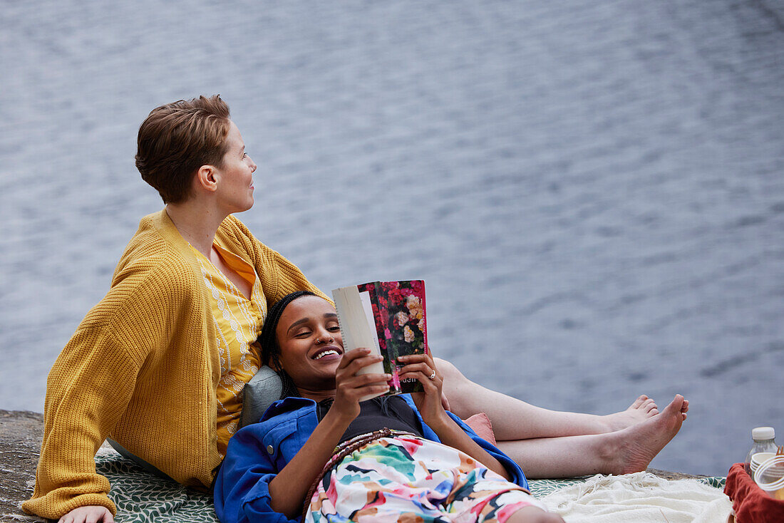 Weibliches Paar liest ein Buch am Fluss