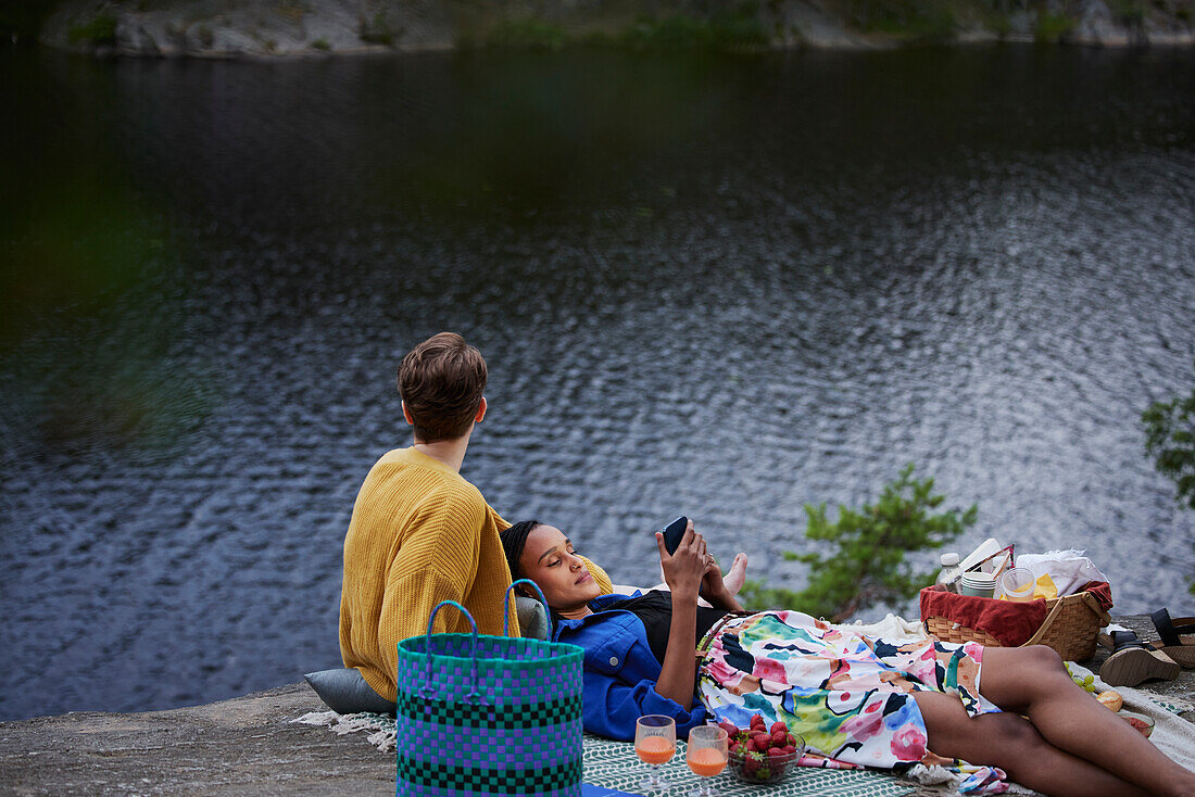 Weibliches Paar beim Picknick am Fluss und beim Telefonieren