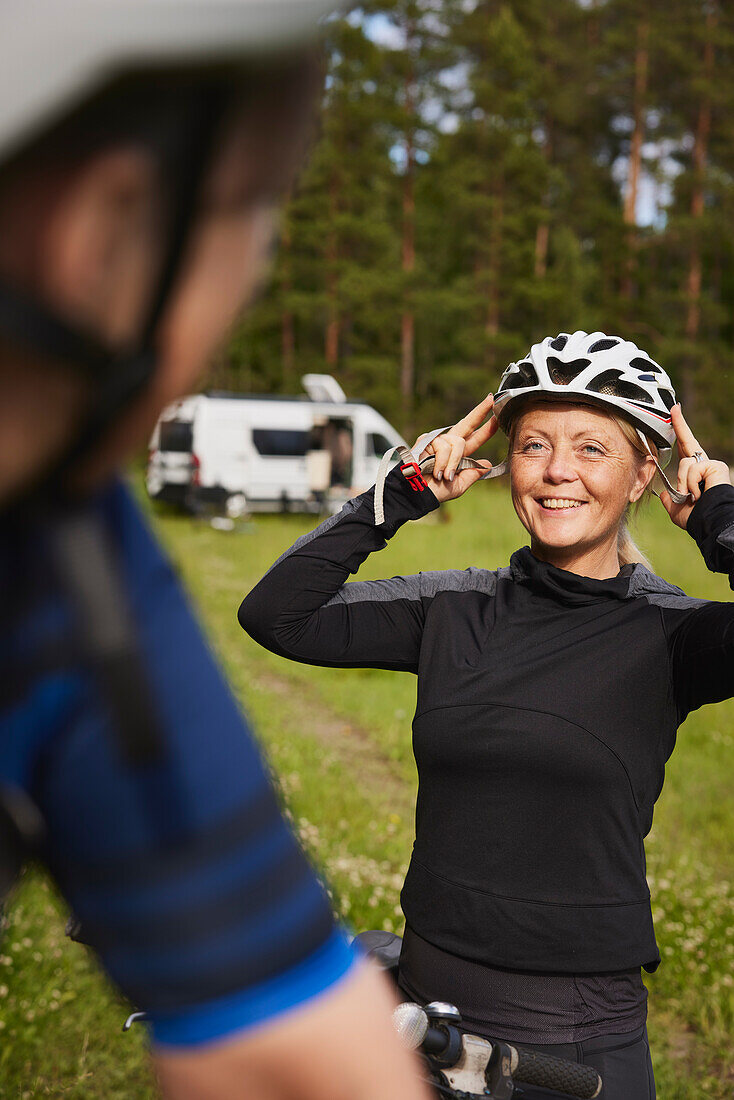 Lächelnde Frau beim Aufsetzen des Fahrradhelms