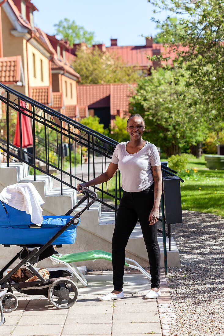 Woman with baby stroller in front of house