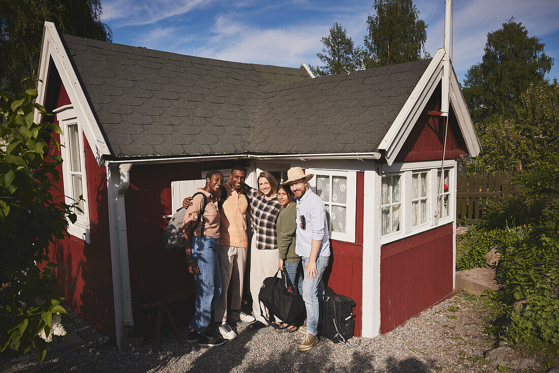 Smiling friends standing in front of wooden house