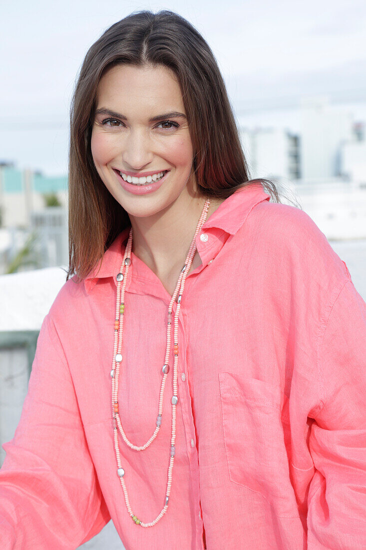 A young woman wearing a salmon-coloured shirt with a pearl necklace